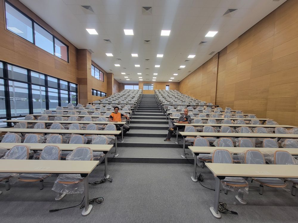 Tiered lecture hall with fixed tables and chairs and a center stair