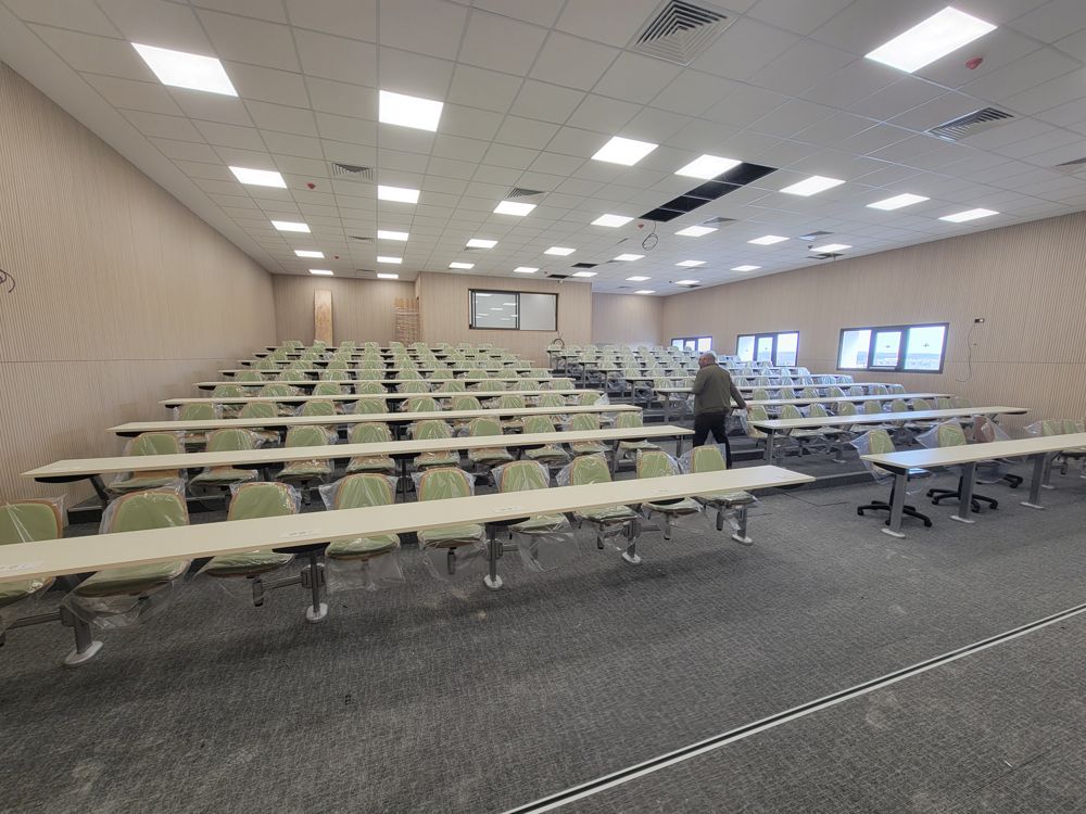 Long lecture hall with rows of fixed tables and seating