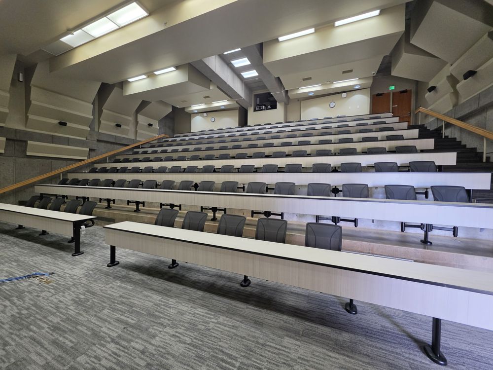 Tiered lecture hall with white tables and gray swivel seats